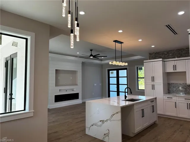Kitchen featuring ceiling fan, pendant lighting, sink, a center island with sink, and a large fireplace