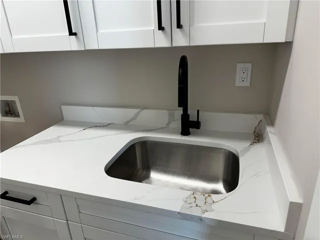 Interior details with white cabinetry, light stone countertops, and sink
