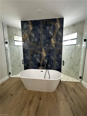 Bathroom with hardwood / wood-style floors, tile walls, and separate shower and tub