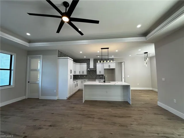 Kitchen featuring ceiling fan, white cabinets, tasteful backsplash, a center island with sink, and wall chimney range hood