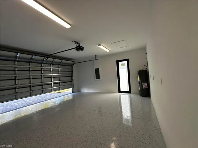 Garage with water heater, electric panel, and a garage door opener