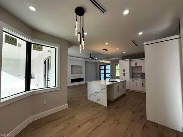 Kitchen with dark wood-type flooring, an island with sink, white cabinets, pendant lighting, and sink