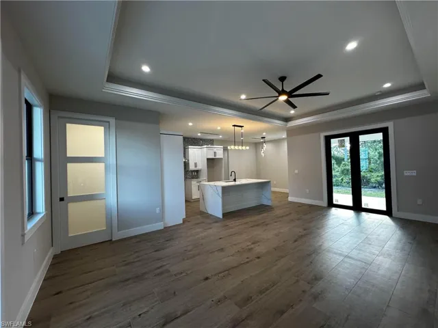 Unfurnished living room featuring dark hardwood / wood-style flooring, sink, a raised ceiling, crown molding, and ceiling fan