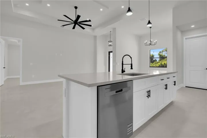 Kitchen featuring a large center island with solid-surface countertop, white shaker-style cabinetry, matte black hardware, stainless steel dishwasher, and high-arc pull-down faucet beneath recessed and pendant lighting
