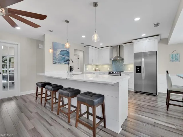 Kitchen featuring white cabinets, kitchen peninsula, appliances with stainless steel finishes, and wall chimney exhaust hood