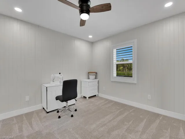 Home office with wooden walls, light colored carpet, and ceiling fan