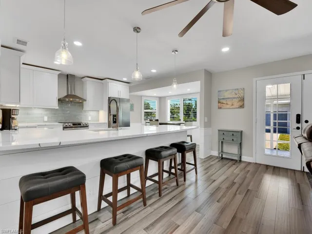 Kitchen featuring white cabinetry, a kitchen bar, wall chimney exhaust hood, and light hardwood / wood-style floors