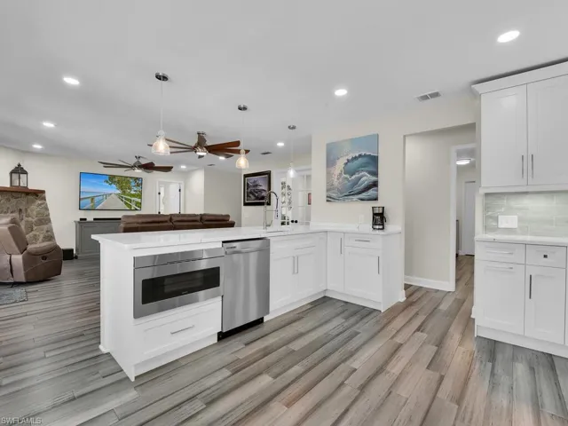 Kitchen with light hardwood / wood-style flooring, hanging light fixtures, appliances with stainless steel finishes, and white cabinets