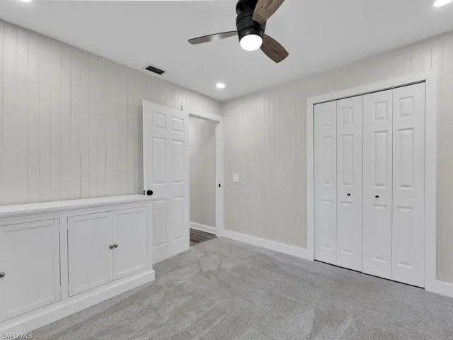 Unfurnished bedroom featuring light carpet, ceiling fan, wooden walls, and a closet