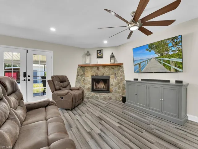 Living room featuring a stone fireplace, light wood-type flooring, french doors, and ceiling fan