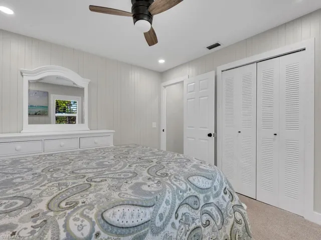 Bedroom featuring light colored carpet, wood walls, ceiling fan, and a closet