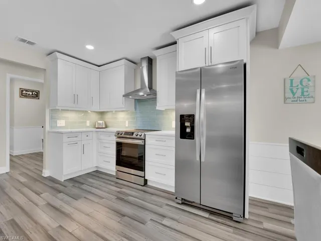 Kitchen with white cabinets, wall chimney exhaust hood, light wood-type flooring, and appliances with stainless steel finishes