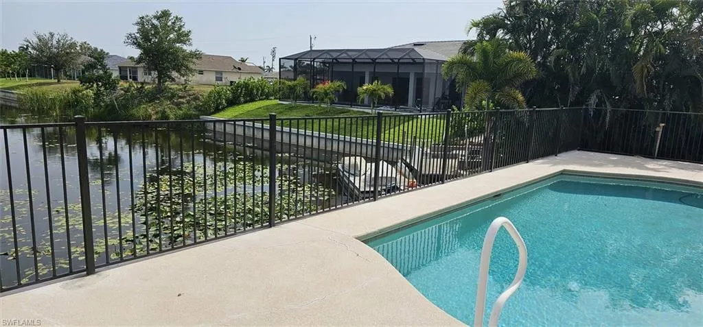 Private swimming pool with a concrete surround, canal frontage with a boat lift, and a black wrought iron fence