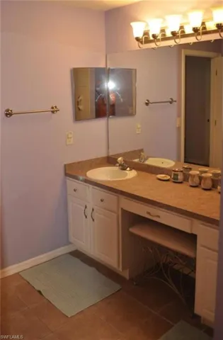 Dual vanity with integrated sinks and countertop, accompanied by white cabinetry and a dedicated vanity seating area