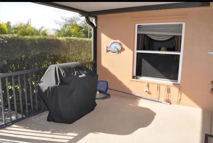 Covered patio with concrete flooring, bordered by a black metal railing and dense hedge