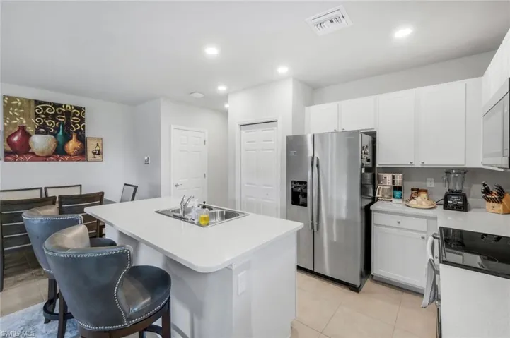 Kitchen featuring appliances with stainless steel finishes, a kitchen island with sink, white cabinets, a kitchen bar, and recessed lighting