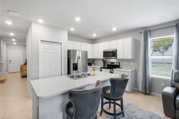 Kitchen featuring stainless steel appliances, white cabinetry, recessed lighting, a kitchen breakfast bar, and a kitchen island with sink