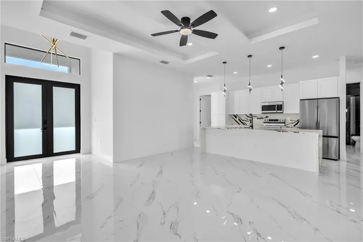 Unfurnished living room featuring french doors, a raised ceiling, ceiling fan, recessed lighting, and light marble finish flooring