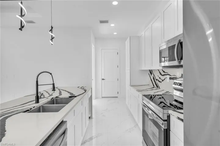 Kitchen with stainless steel appliances, white cabinets, light stone countertops, and light marble finish floors