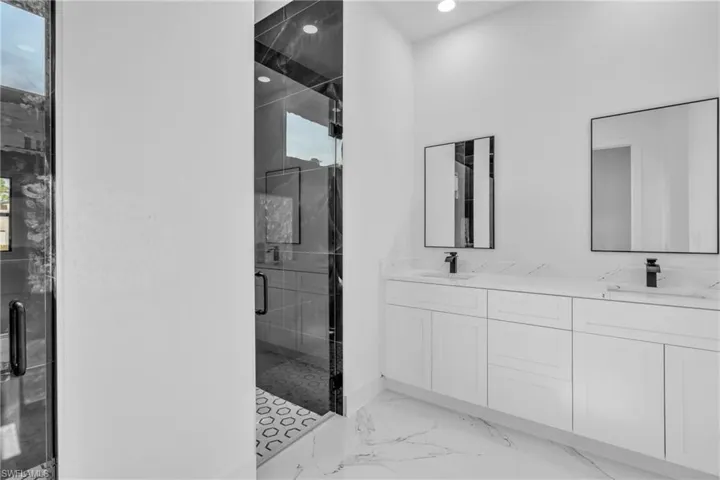 Bathroom with a marble finish shower, double vanity, light marble finish flooring, and recessed lighting