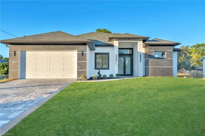 Prairie-style home featuring a shingled roof, a front yard, stucco siding, decorative driveway, and an attached garage