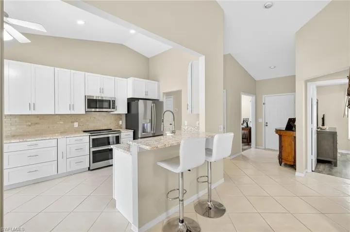Kitchen with high vaulted ceiling, light tile patterned flooring, appliances with stainless steel finishes, tasteful backsplash, and ceiling fan