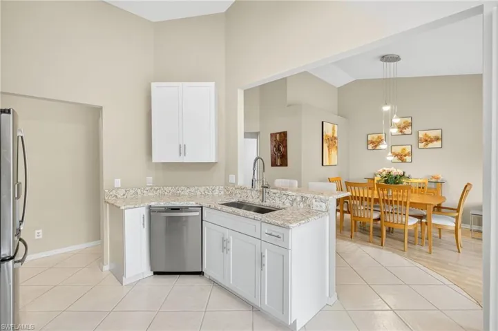 Kitchen with high vaulted ceiling, appliances with stainless steel finishes, light tile patterned floors, white cabinetry, and a peninsula