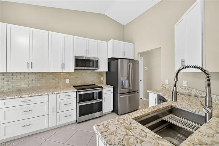 Kitchen featuring light tile patterned floors, appliances with stainless steel finishes, decorative backsplash, white cabinets, and light stone counters