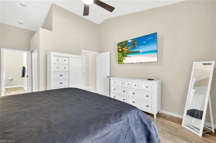 Bedroom with light wood-style floors, connected bathroom, high vaulted ceiling, and a ceiling fan