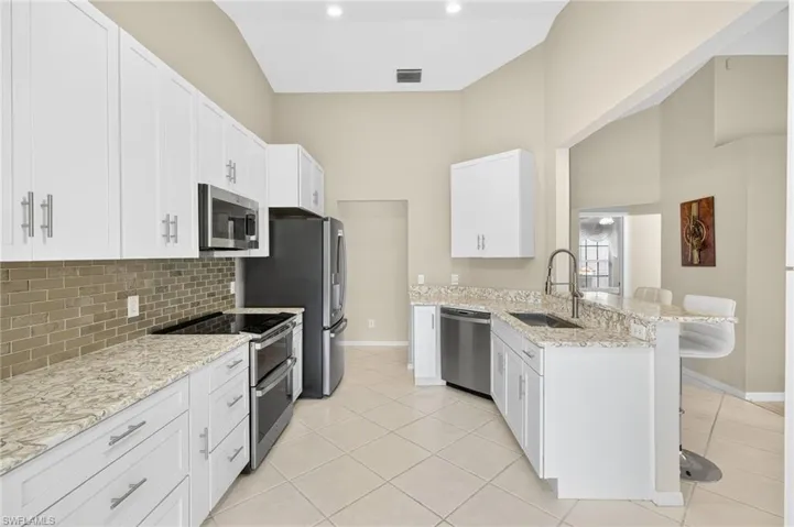 Kitchen with a breakfast bar, appliances with stainless steel finishes, a peninsula, backsplash, and white cabinets