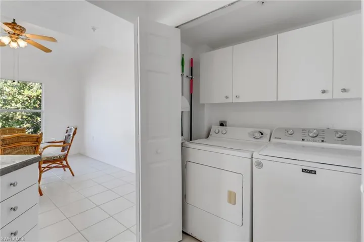 Clothes washing area featuring cabinets, washing machine and dryer, light tile patterned flooring, and ceiling fan