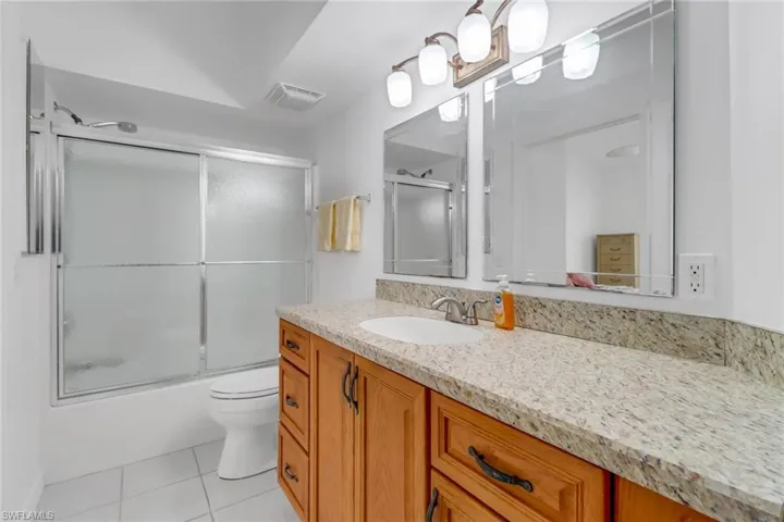 Full bathroom with vanity, bath / shower combo with glass door, tile patterned floors, and toilet