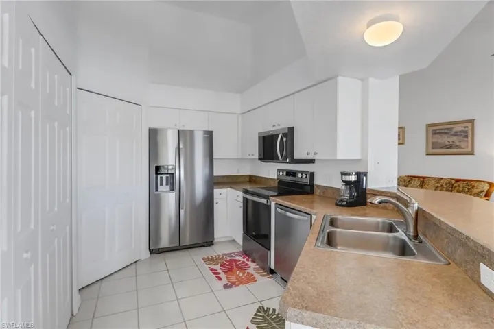 Kitchen with stainless steel appliances, white cabinetry, sink, and light tile patterned floors