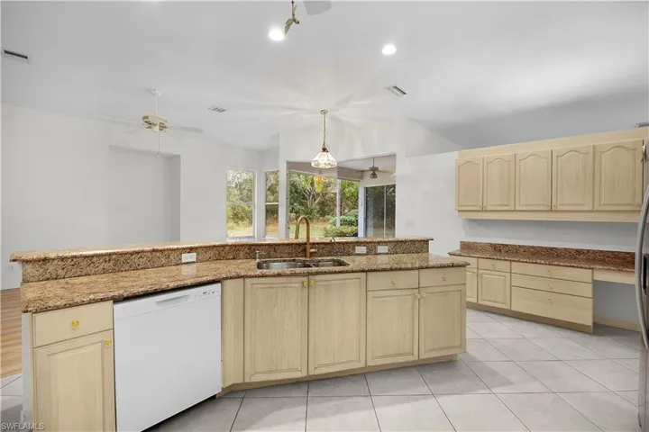 Kitchen featuring light brown cabinets, white dishwasher, light stone countertops, decorative light fixtures, and light tile patterned floors