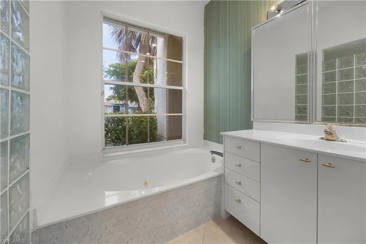 Full bath with a whirlpool tub, vanity, and light tile patterned floors