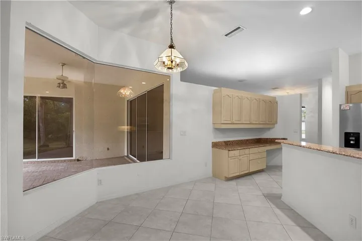 Kitchen with light tile patterned floors, stainless steel fridge with ice dispenser, light brown cabinetry, dark stone counters, and decorative light fixtures