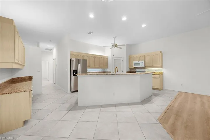 Kitchen featuring light tile patterned floors, stainless steel fridge with ice dispenser, light brown cabinets, a kitchen island with sink, and recessed lighting