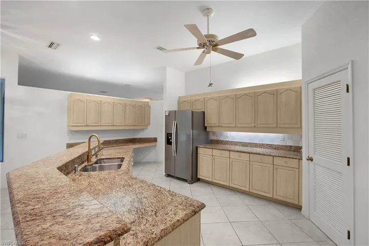 Kitchen with light brown cabinets, stainless steel fridge, a ceiling fan, and light stone countertops