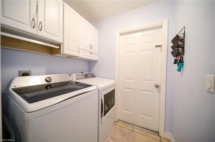 Laundry area featuring white shaker-style wall cabinetry, a six-panel door, and tiled flooring