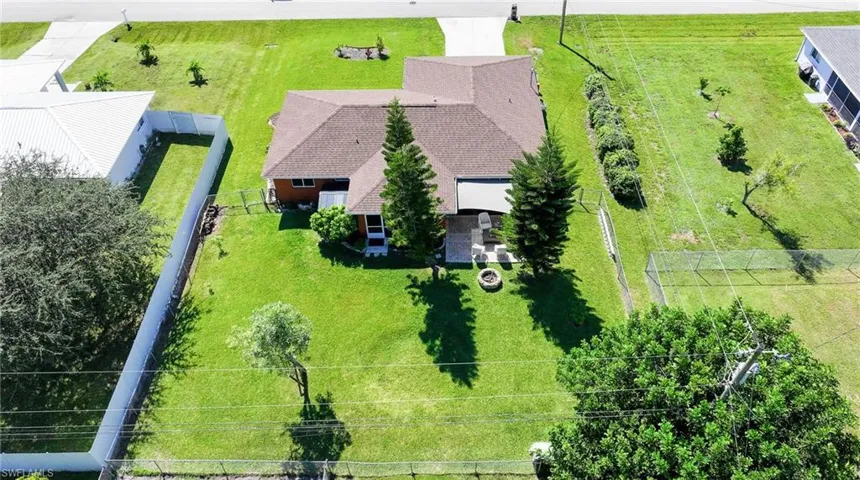 Aerial perspective of a property featuring an expansive lawn, concrete patio, circular stone fire pit, and mature pine trees