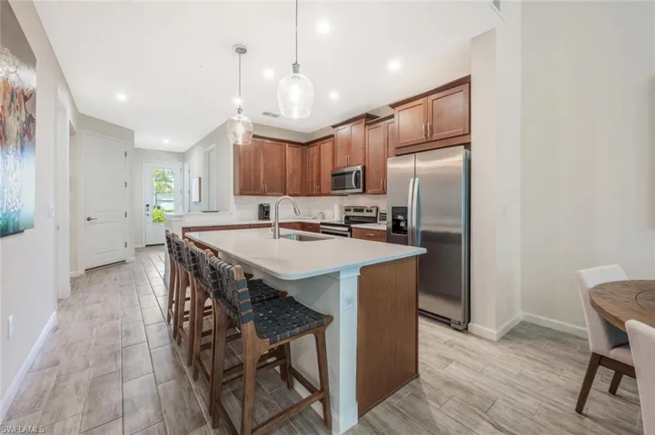 Kitchen with appliances with stainless steel finishes, light countertops, an island with sink, a kitchen breakfast bar, and brown cabinetry