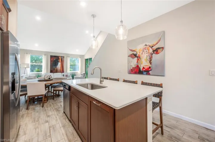 Kitchen featuring appliances with stainless steel finishes, light countertops, a kitchen island with sink, vaulted ceiling, and a kitchen bar