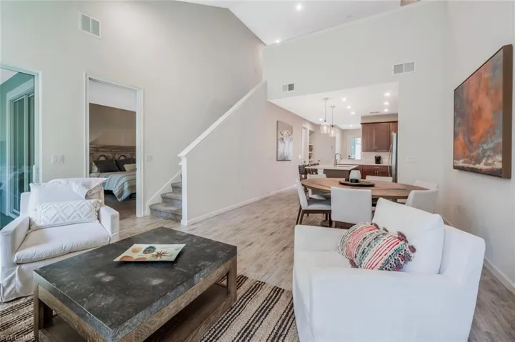 Living room featuring high vaulted ceiling, stairway, light wood finished floors, and recessed lighting