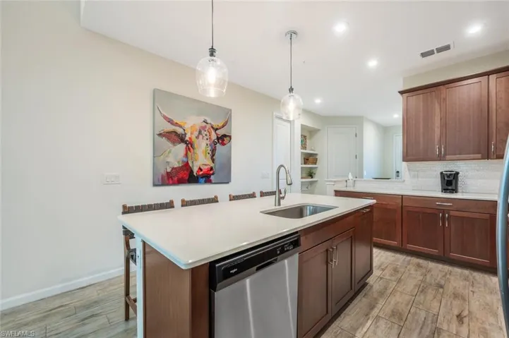 Kitchen with stainless steel dishwasher, light wood-style floors, light countertops, hanging light fixtures, and a kitchen bar