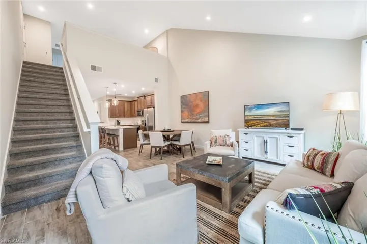 Living room featuring stairs, light wood-style floors, recessed lighting, and a towering ceiling