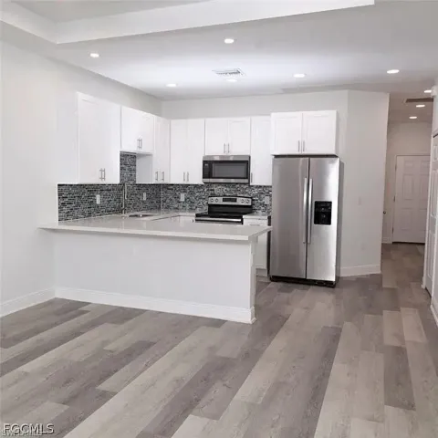 Kitchen featuring white shaker-style cabinetry, stainless steel appliances, a mosaic tile backsplash, and light-toned countertops