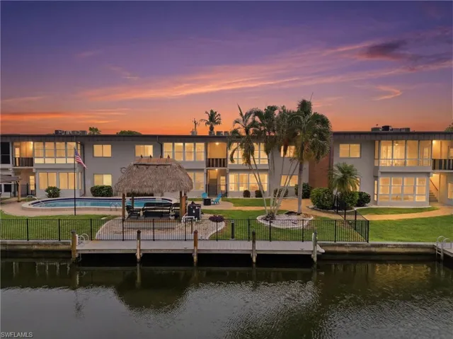 Waterfront multi-story building featuring a dock, in-ground swimming pool, and a thatched-roof tiki hut