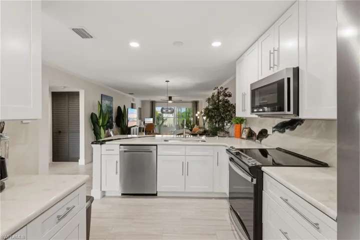 Modern kitchen featuring white cabinetry, light-toned countertops, stainless steel appliances, and wood-finish tile flooring