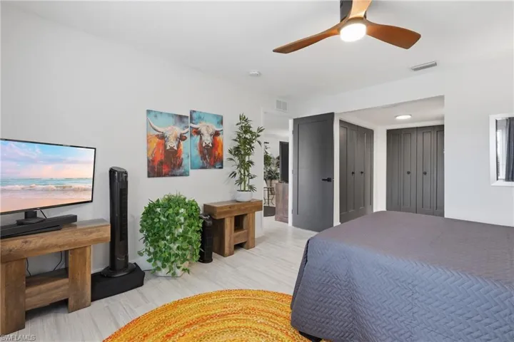 Room featuring wood-finish flooring, a contemporary ceiling fan with integrated lighting, and dark-paneled doors with black hardware