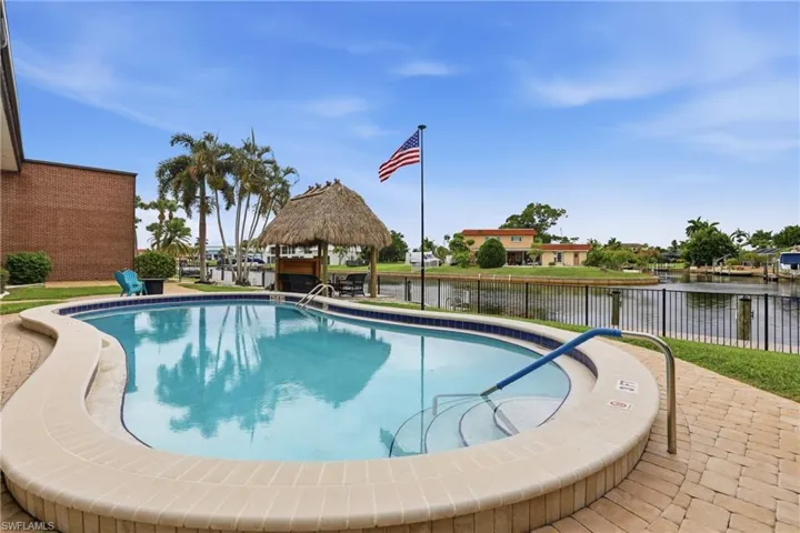 Resort-style pool area featuring a freeform swimming pool with integrated steps, a tiki hut, and paver decking